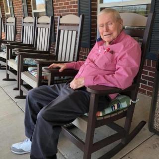 An elderly man sitting in a rocking chair on a porch.