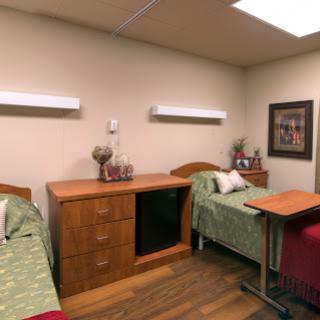 A shared hospital room featuring two patient beds, wooden furniture, and soft lighting.