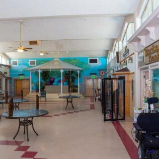 An empty indoor space featuring tables, chairs, a gazebo, and a mural on the wall.