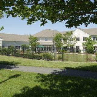 A two-story building surrounded by trees and a well-maintained lawn on a sunny day.
