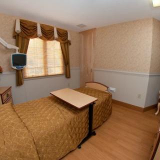 A hospital room with a single bed, TV, and wooden flooring.