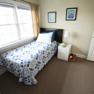 A cozy bedroom with a single bed, blue and white bedding, and plenty of natural light from the window.