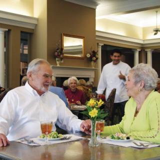 An elderly couple enjoying a meal together in a restaurant, with a waiter approaching their table.