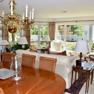 A spacious living and dining area with a wooden table, elegant chandelier, and large windows providing ample natural light.
