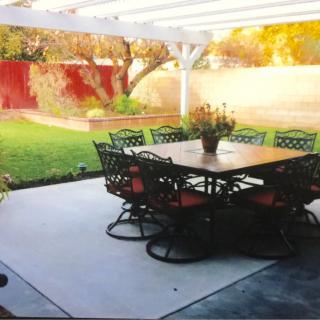 An outdoor patio featuring a dining set under a pergola, overlooking a garden.