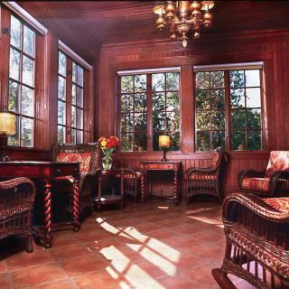 A cozy room with wooden paneling, wicker furniture, and abundant natural light streaming through large windows.