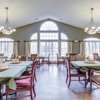 A bright and spacious dining room with multiple tables and chairs, illuminated by natural light streaming through large windows.