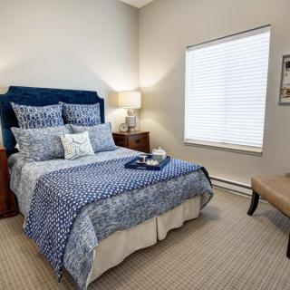 A cozy bedroom with a neatly made bed, bedside tables with lamps, and a window letting in natural light.