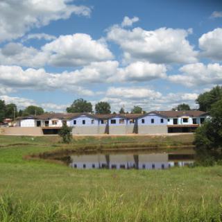 A serene view of residential houses reflected in a pond under a cloudy sky.