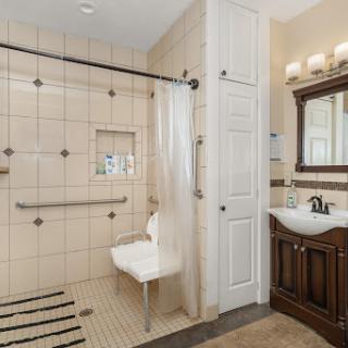A spacious bathroom featuring a wheelchair accessible shower with a foldable seat and elegant vanity.