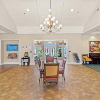 A well-lit dining room with a chandelier, wooden flooring, and a central table surrounded by chairs.