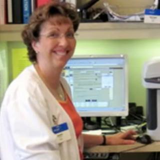 A woman in a lab coat working at a computer in an office.