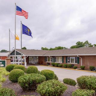 A modest office building featuring multiple flags and well-maintained landscaping under a cloudy sky.