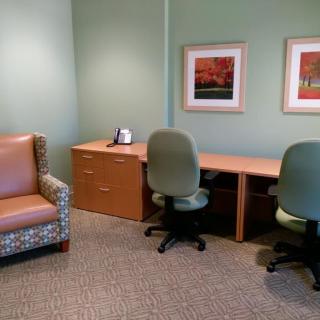 A simple office space with a desk, chairs, and artwork on the walls.