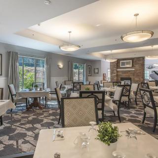 An elegant dining room interior with neatly arranged tables and chairs, featuring large windows and stylish lighting.