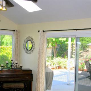 A bright living room with a piano and candles, featuring large sliding glass doors that open to a patio.