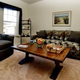 A cozy living room featuring a comfortable sofa and a wooden coffee table adorned with flowers, set against a backdrop of neutral tones and tasteful decor.