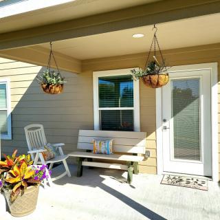 A cozy porch with a bench, chair, and hanging plants on a sunny day.