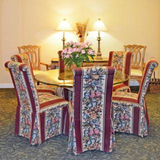 A cozy dining area featuring a round table surrounded by chairs with floral upholstery, adorned with a floral centerpiece and illuminated by warm lighting.