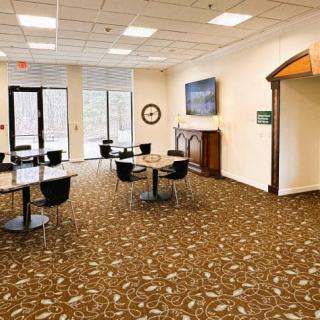 A spacious lobby area with tables and chairs, featuring a television and large windows.