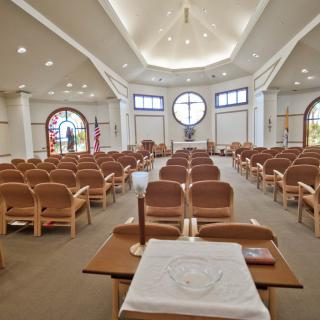 Interior view of a church with pews and altar, featuring stained glass windows.