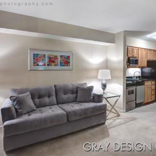 A modern living space featuring a gray sofa, decorative artwork, and an open kitchen area.