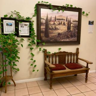 A cozy corner with a wooden bench, adorned with red cushions, framed by leafy green vines and wall art depicting a serene landscape.