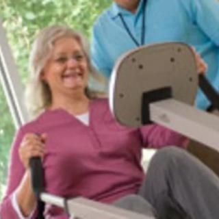 A woman exercising on a machine with assistance from a healthcare professional.