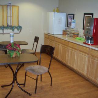 A cozy break room with tables and chairs, featuring a refrigerator and coffee machine.