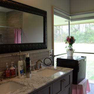 A bathroom with a marble countertop and vanity, a large mirror, and a window adorned with flowers.