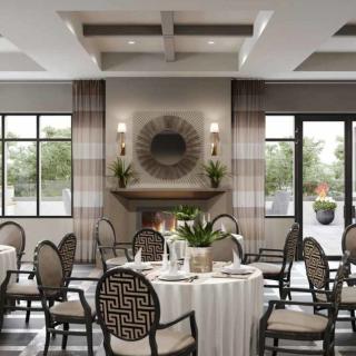 An elegantly designed dining room with neatly arranged tables and chairs, featuring a central fireplace and ample natural light.