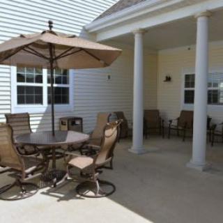 A cozy outdoor patio with a table, chairs, and an umbrella, beside a house porch with columns.