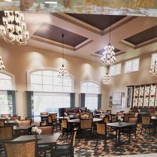 A spacious dining area featuring elegant chandeliers, multiple tables and chairs, and large windows.