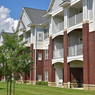 A modern apartment building with brick and siding exterior, featuring balconies and a well-maintained lawn.