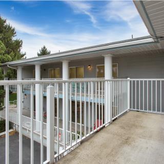 A view from a balcony with white railings overlooking a modern building and trees under a blue sky.