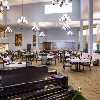 A spacious and elegant dining room featuring a grand piano and multiple chandeliers.