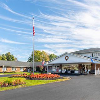 A motel with neatly landscaped grounds and an American flag flying on a flagpole under a blue sky with wispy clouds.