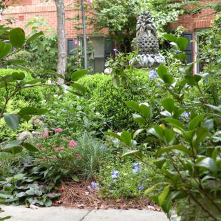 A lush garden with diverse greenery and a decorative sculpture in the background.