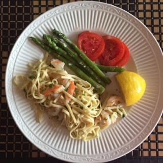 A delightful plate featuring pasta with shrimp, accompanied by asparagus, fresh tomato slices, and a lemon wedge.