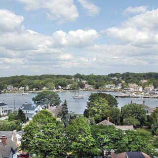 A scenic view of a riverside town with lush green trees and houses under a partly cloudy sky.
