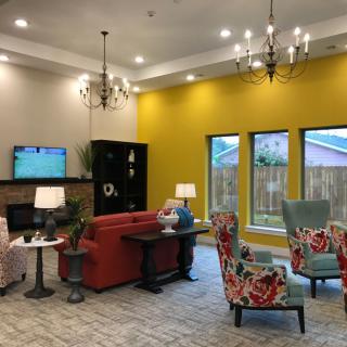 A cozy living room with vibrant decor, featuring a red sofa, patterned chairs, and a striking yellow accent wall.