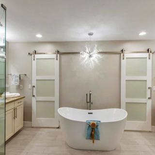A modern, minimalist bathroom featuring a freestanding bathtub with elegant lighting and glass sliding doors.