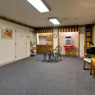 A cozy basement featuring a table and chairs, surrounded by artwork, shelves, and a small kitchenette.