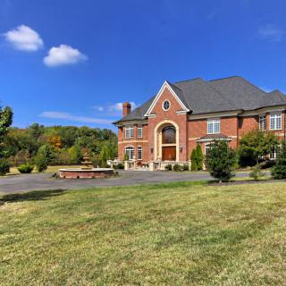 A large brick mansion with a spacious lawn under a clear blue sky.