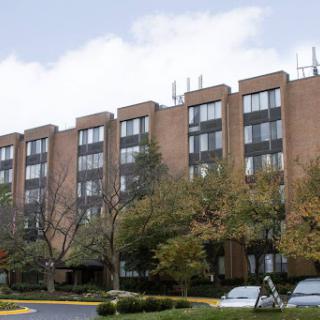 A multi-story apartment building surrounded by trees under a cloudy sky.