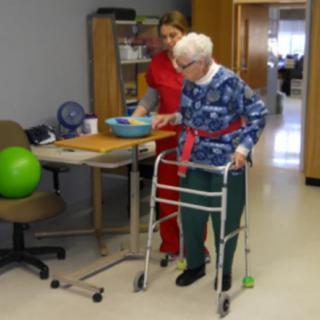 An elderly person receives assistance with walking from a healthcare professional in a rehabilitation setting.