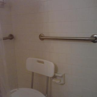 A bathroom with grab bars and a chair, designed for accessibility.