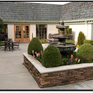 A beautifully landscaped courtyard with a central fountain, surrounded by neatly trimmed shrubs and outdoor seating.