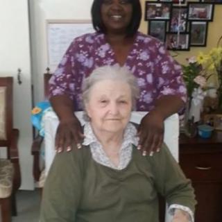 A caregiver standing behind an elderly woman seated indoors.