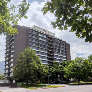 A high-rise building surrounded by trees under a partly cloudy sky.